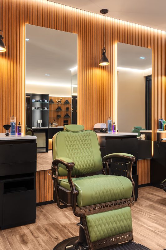 An olive barber chair at a lit mirror inside On the Mark